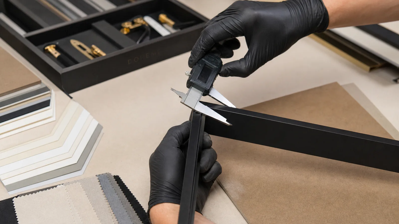Technician measuring a black custom display frame profile with a digital caliper during sample review